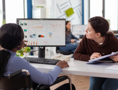 Businesswoman discussing with invalid disabled paralysed african woman company development plan. Handicapped black leader explainig project strategy to manager corporate in strat up business office.