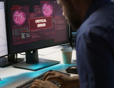 Programmer seeing red critical error popup on computer display in data center, panicking. African american man in server hub spamming keyboard buttons after receiving error, camera A