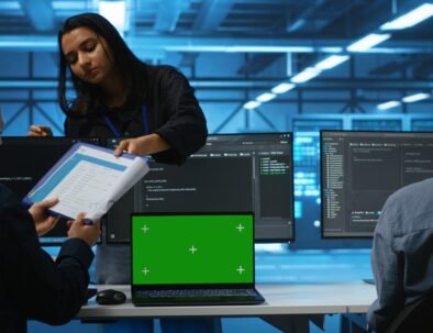 Green screen laptop in data center in front of manager and IT support specialists working together, supervising server rows. Team leader and employees overseeing supercomputers using mockup notebook